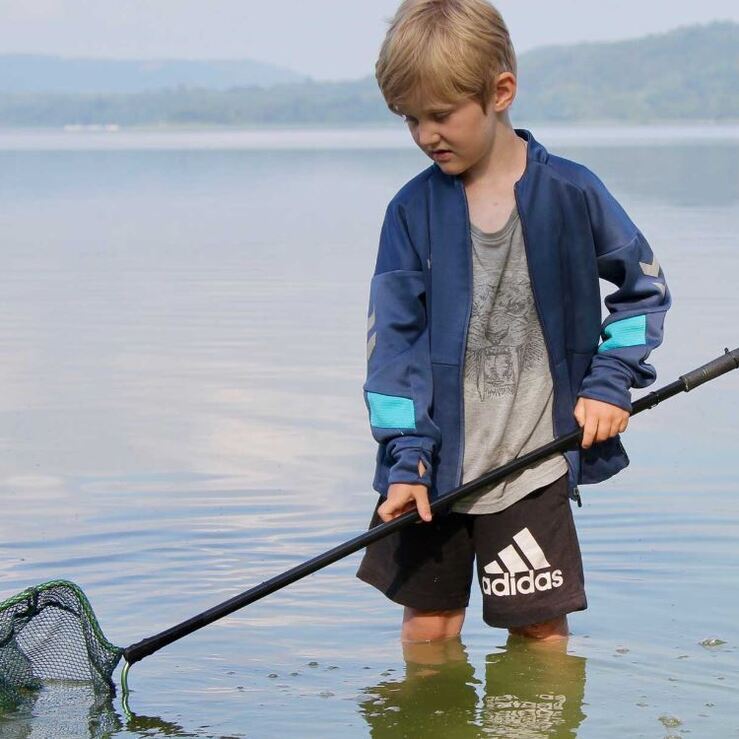 Dreng viser fiskenet frem ved sø.