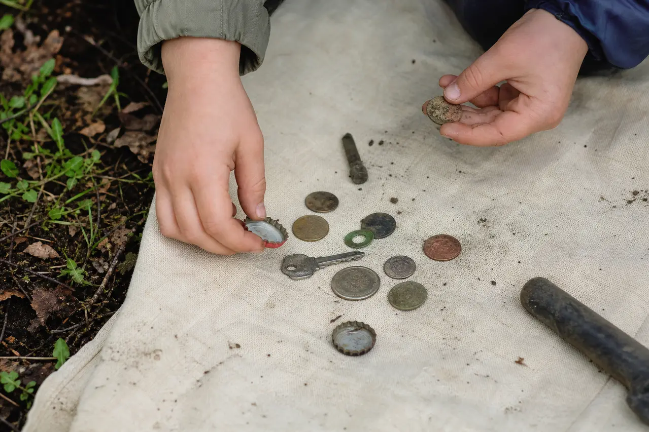 Hænder sorterer små metalfund på stof